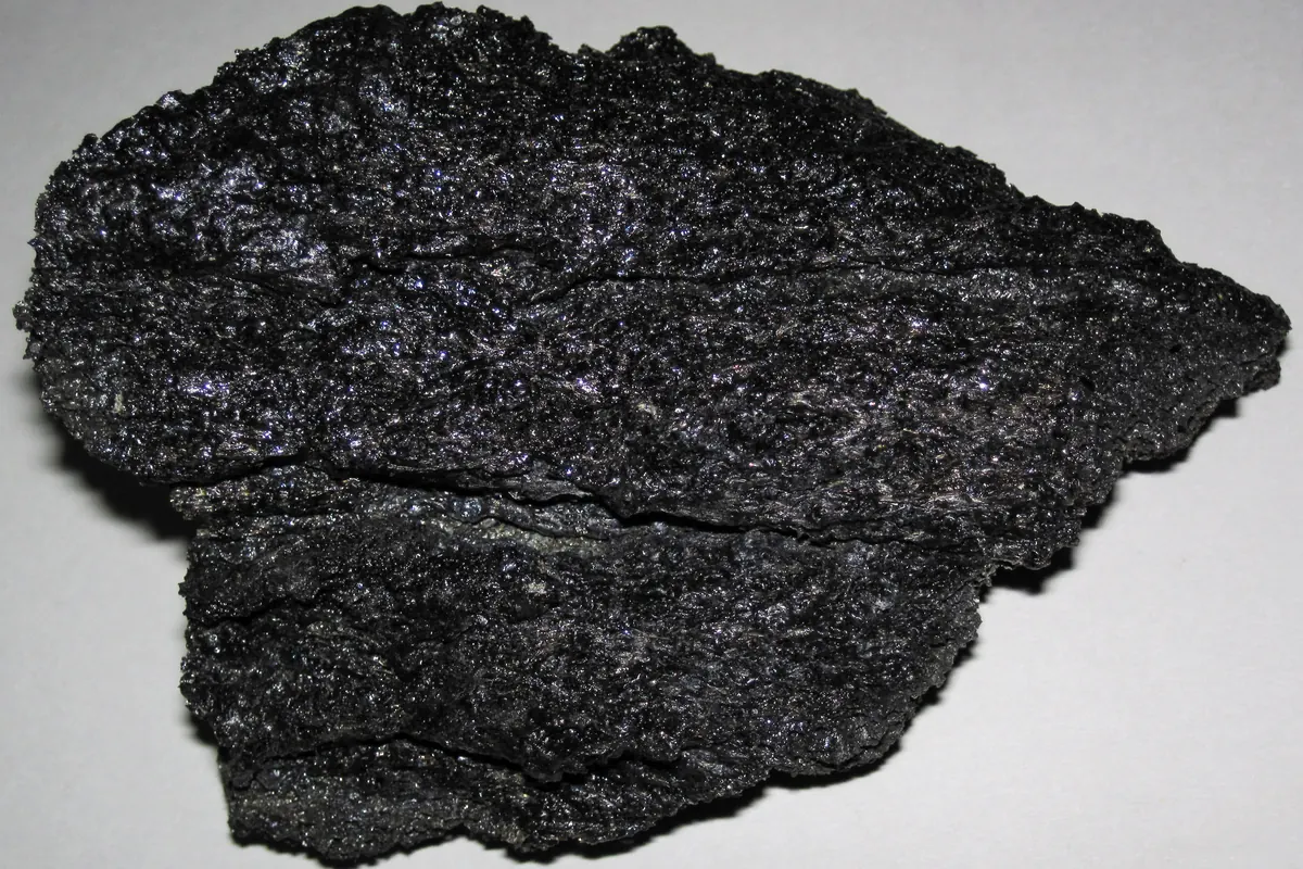 A shiny black piece of basalt lava from Iceland with a rough, glittering surface, photographed on a grey background