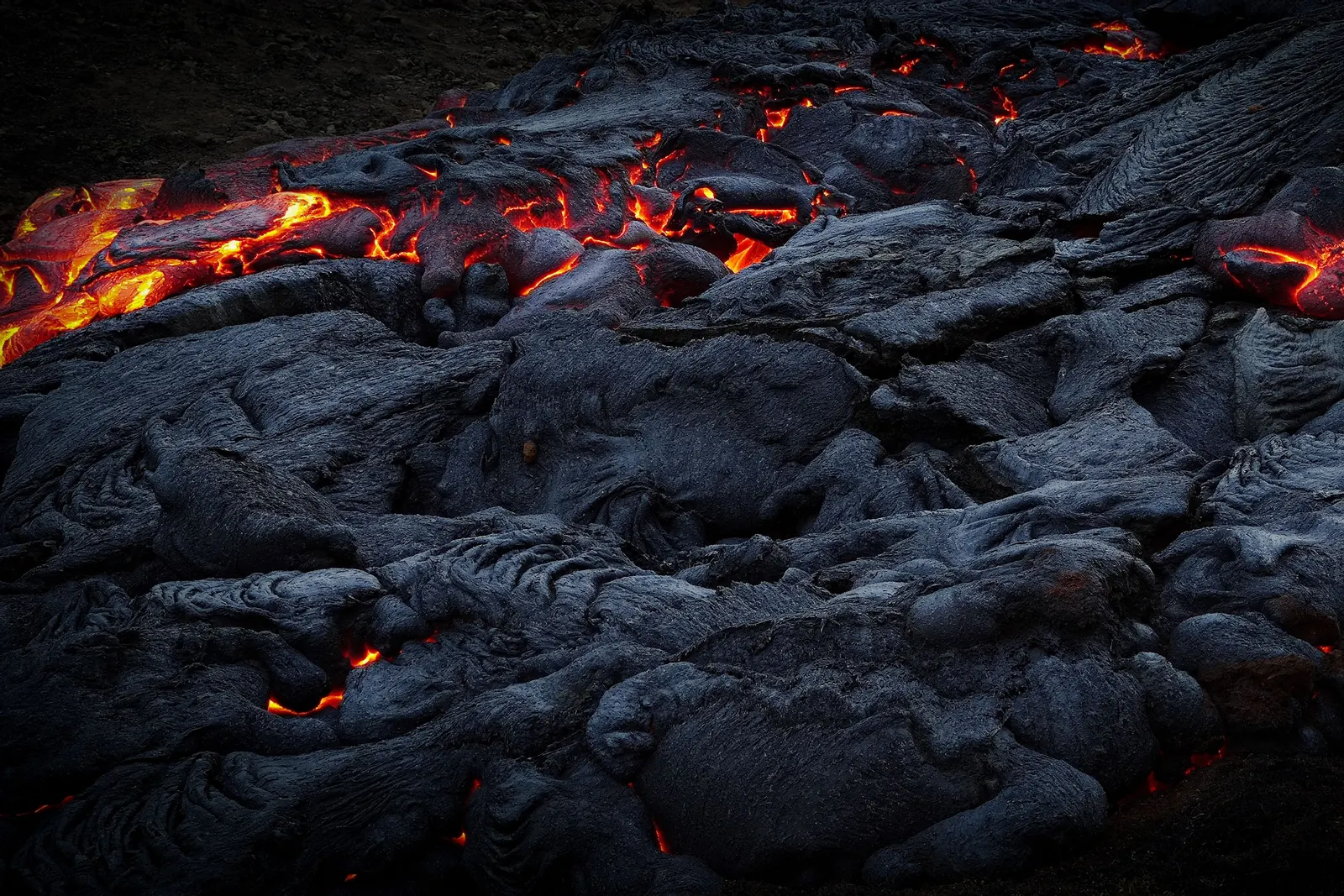 Bright orange lava glowing between plates of black, cooled rock on an Icelandic lava flow